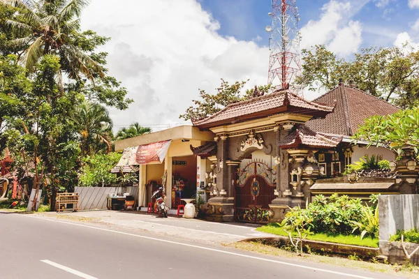 BALI, INDONESIA - 30 de enero de 2013. La vida callejera habitual en Bali. Pequeña tienda y casa con detalles arquitectónicos tradicionales - puerta tallada en piedra . — Foto de Stock