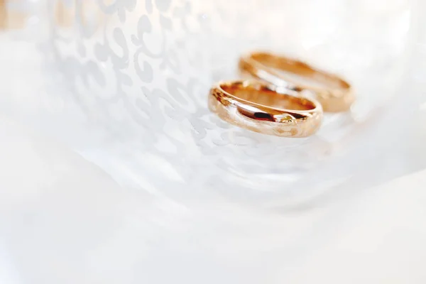 Wedding golden rings in transparent glass. Symbol of love and marriage. Creative picture with glass glittering in the sunlight. — Stock Photo, Image