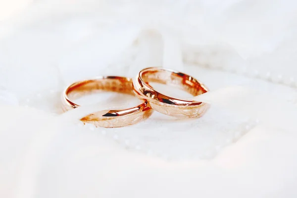 Golden wedding rings on white silk background. Wedding details. Symbol of love and marriage.