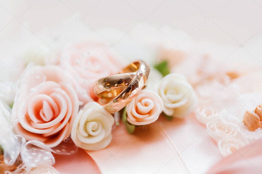 Pair of golden wedding rings on lace fabric with roses and bow. Wedding textile details. Symbol of love and marriage.