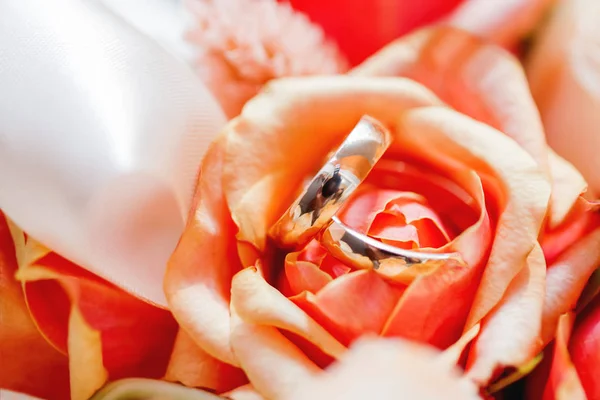 Golden wedding rings lie inside orange rose flower in the bouquet. Symbol of love and marriage. — Stock Photo, Image