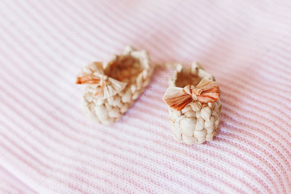 Cute tiny sandals made of straw, ancient traditional russian type of footwear. Natural booties for baby girl with a bow on pink knitted fabric background.