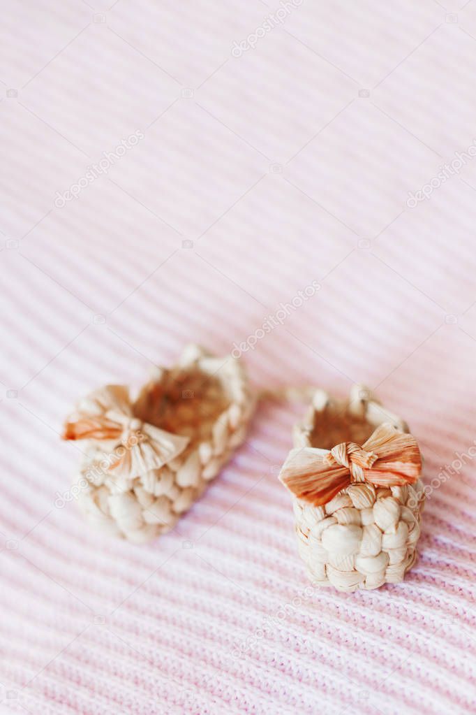 Cute tiny sandals made of straw, ancient traditional russian type of footwear. Natural booties for baby girl with a bow on pink knitted fabric background. Place for text.