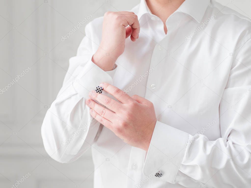 Man in white shirt adjusts his cufflinks. Groom is getting ready for wedding ceremony.