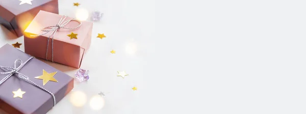 Regalos navideños. Regalos envueltos en papel rosa pálido y violeta con cintas de plata y lazo. Estrellas confeti, bombillas bokeh y espacio de copia en blanco . —  Fotos de Stock