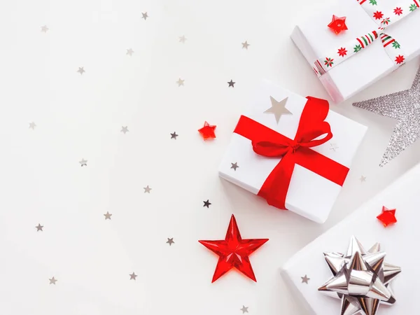 Fondo de Navidad y Año Nuevo con regalos en papel de regalo blanco. Regalos navideños con cinta roja y plateada y lazos. Copiar espacio con confeti estrella de plata . —  Fotos de Stock