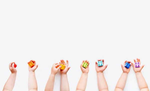 Los niños sostienen bloques constructores de color arco iris en puños. Niños manos con ladrillos juguete sobre fondo blanco. Juguetes educativos coloridos. Piso tendido, vista superior . — Foto de Stock