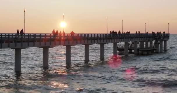 Silhuetas de pessoas andando no cais contra o pôr do sol. As pessoas locais estão pescando, os turistas estão andando antes de ir para a cama. Zelenogradsk, Rússia . — Vídeo de Stock