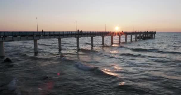 Silhouetten von Menschen, die auf der Seebrücke gegen den Sonnenuntergang gehen. Einheimische fischen, Touristen gehen vor dem Schlafengehen spazieren. zelenogradsk, Russland. — Stockvideo