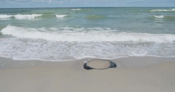 Die Wellen trafen den Strand mit einem alten Autoreifen, der im Sand vergraben war. zelenogradsk, Russland. — Stockvideo