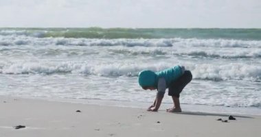 Yelekli çocuk deniz kenarındaki kumla oynuyor..