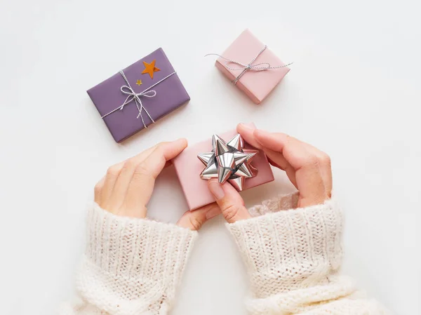 Mujer está decorando regalo de Navidad con arco de plata brillante. Regalos de Año Nuevo en papel de regalo rosa y violeta con confeti estrella brillante y cintas. Vista superior, plano . —  Fotos de Stock