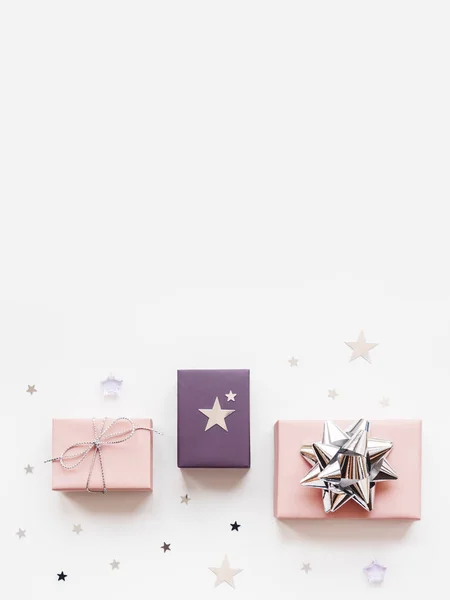 Bannière avec cadeaux de vacances. Cadeaux enveloppés dans du papier rose pâle et violet avec rubans argentés et noeud. Confettis étoiles et espace de copie blanche. Vue de dessus, plan plat . — Photo