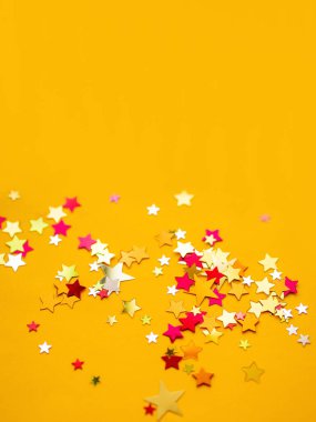 Renkli yıldız konfetiyle sarı tatil geçmişi. Noel ve Yeni Yıl kartları için iyi bir geçmiş.