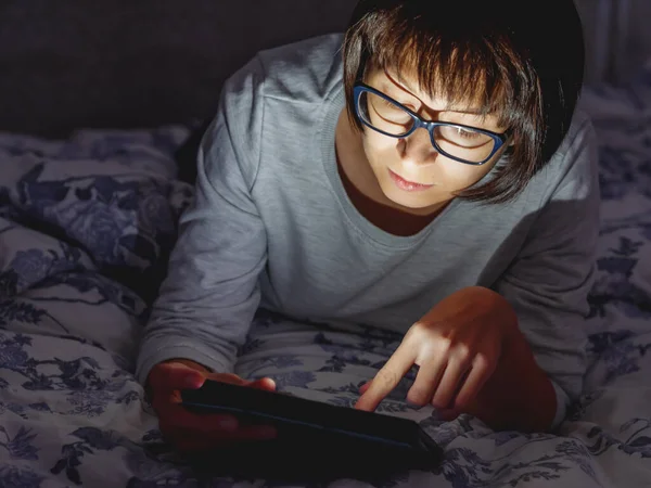 Женщина в очках лежит в постели с табличкой в темной комнате. Она трогает экран. Ночью спать . — стоковое фото