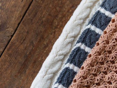 Eski püskü ahşap arka planda gri, beyaz ve bej örülmüş kazaklar. Üst manzara, düz uzanma.