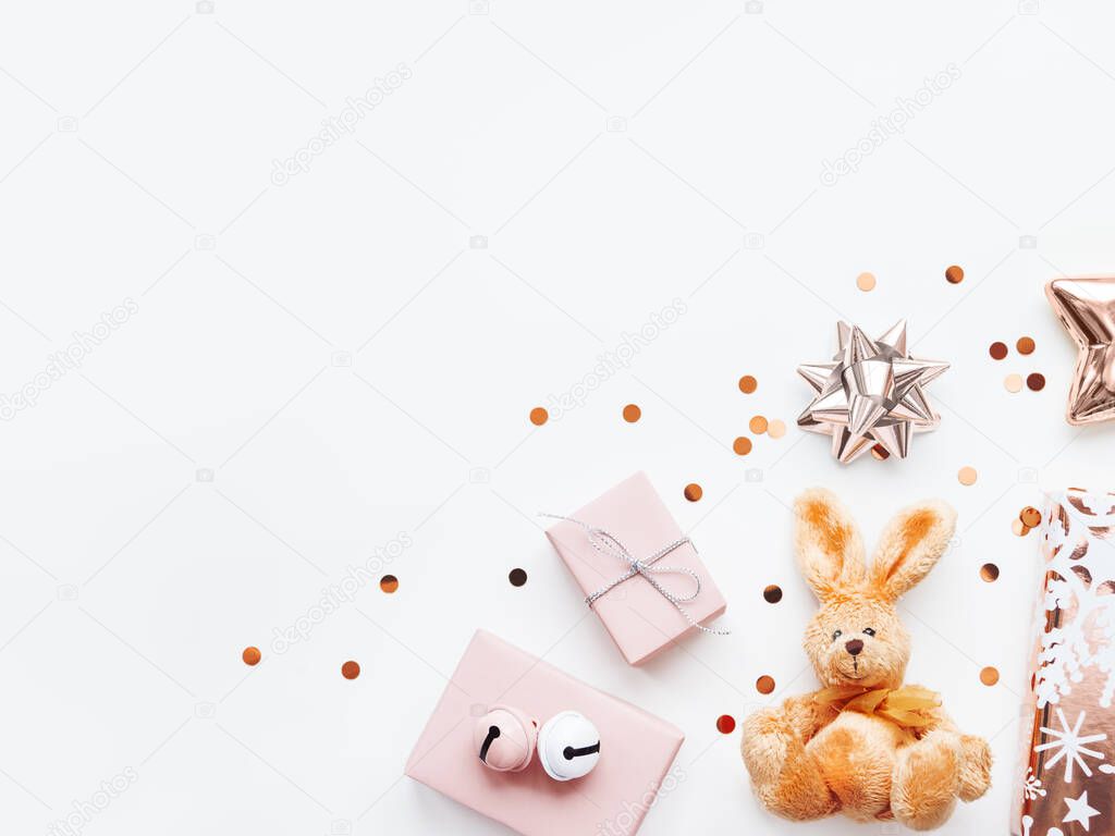 Holiday presents in shadows of pink - fluffy toy rabbit, gifts with decorative bells, sparkling confetti, golden star. Presents for little girl.