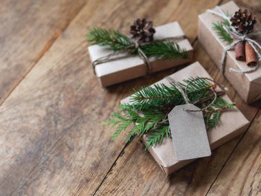 Noel hediyeleri el sanatları kağıdına sarılmış doğal köknar ağacı ve thuja dallarıyla süsleme olarak. Elle yapılmış ahşap masa, yeni yıl hediyeleri..
