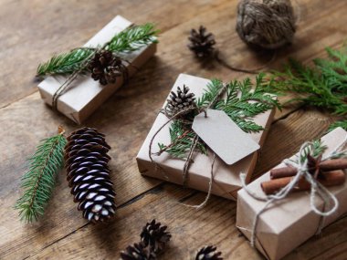 Noel hediyeleri el sanatları kağıdına sarılmış doğal köknar ağacı ve thuja dallarıyla süsleme olarak. Elle yapılmış ahşap masa, yeni yıl hediyeleri..