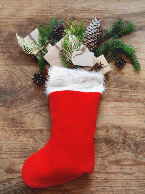 Noel Baba 'da Noel hediyeleri kırmızı çorap. Köknar ağacı dallarıyla el sanatları kağıdında hediyeler ve ahşap arka planda açık etiket.