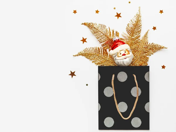 Las plumas doradas brillantes y el Papá Noel decorativo sobresalen de la bolsa de regalo negra con círculos de plata. Regalo de Año Nuevo con decoraciones para árbol de Navidad. Vista superior, plano . — Foto de Stock