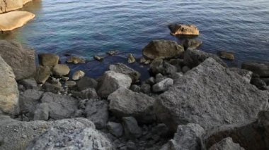 Deniz sörfü. Novy Svet köyündeki Golitsyn yolu yakınlarındaki kayalık sahilde sakin dalgalar esiyor. Kırım.