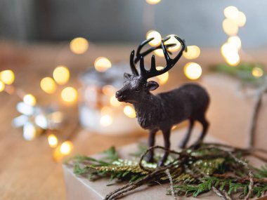 Eski ahşap arka planda Noel hediyeleri. Geyik figürü, yeni yıl hediyelerini ağaç dallarıyla el sanatları kağıdına koyar..