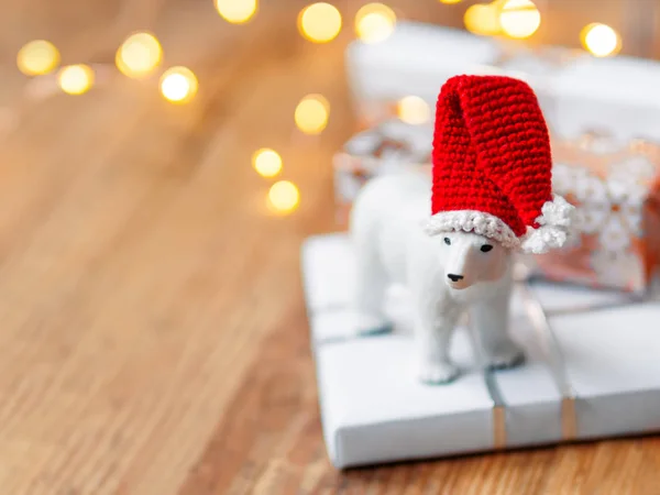 Christmas presents on shabby wooden background. Cute polar bear in Santa's hat standing on New Year gifts in white and golden paper. — Stock Photo, Image