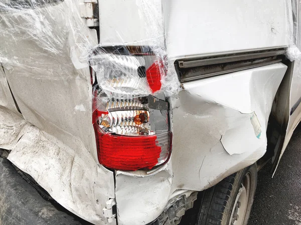 Samochód po wypadku. Złamany zderzak i reflektor. Biały samochód z wgnieceniami pokrytymi folią. — Zdjęcie stockowe