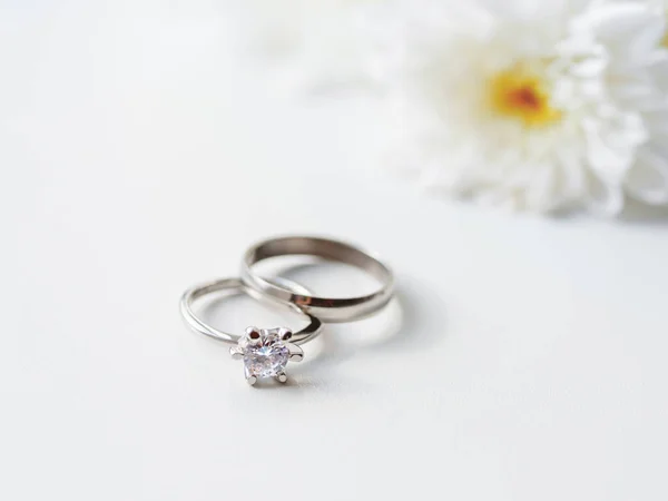 Obrączki ślubne i zaręczynowe z diamentem z białym kwiatem rumianku. Symbol miłości i małżeństwa na białym tle. — Zdjęcie stockowe