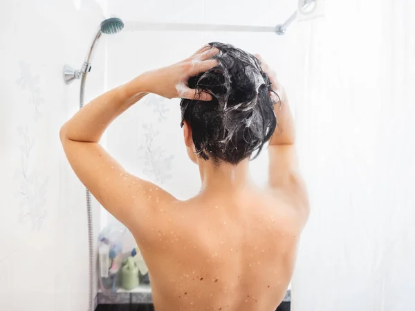 Mulher nua com cabelo curto toma um banho. A mulher lava o cabelo com champô. Banheiro branco . — Fotografia de Stock