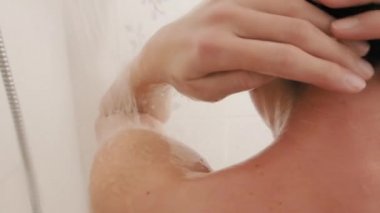 Naked woman takes a shower. Woman washes her short hair with shampoo. Slow motion video in white bathroom.