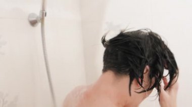Naked woman takes a shower. Woman washes her short hair with shampoo. Slow motion video in white bathroom.