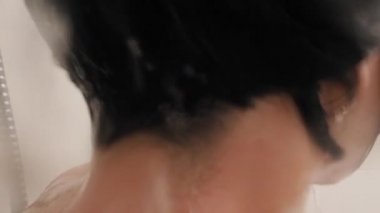 Naked woman takes a shower. Woman washes her short hair with shampoo. Slow motion video in white bathroom.