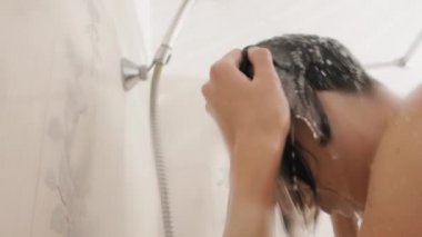 Naked woman takes a shower. Woman washes her short hair with shampoo. Slow motion video in white bathroom.