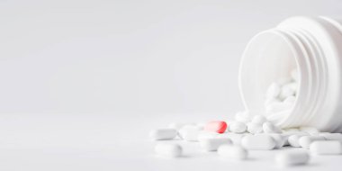 Kırmızı haplı beyaz haplar plastik kavanozdan dökülmüş. Kopya alanı olan beyaz arkaplan üzerindeki ilaç kapsülleri. 