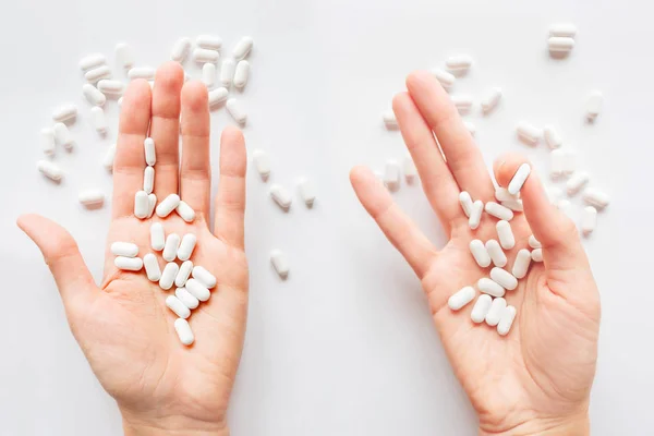 Palm hands full of white scattering pills. Capsules with medicines on light background. Flat lay, top view.