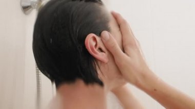 Naked woman takes a shower. Woman washes her short hair with shampoo. Slow motion video in white bathroom.