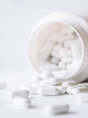 Plastik bir kavanozdan beyaz haplar döküldü. Beyaz arkaplan üzerindeki ilaç kapsülleri.