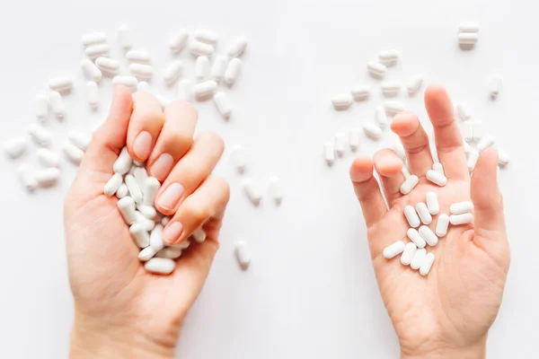 Palm hands full of white scattering pills. Woman gripes hand with capsules with medicines on light background. Flat lay, top view.