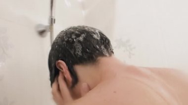 Naked woman takes a shower. Woman washes her short hair with shampoo. Slow motion video in white bathroom.