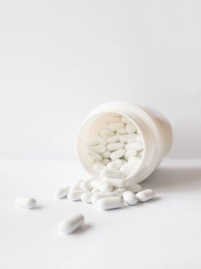 Plastik bir kavanozdan beyaz haplar döküldü. Kopya alanı olan beyaz arkaplan üzerindeki ilaç kapsülleri.
