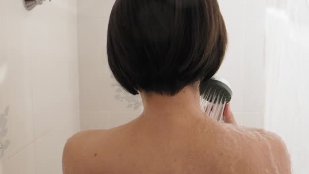 Nahá žena se sprchuje. Žena si myje krátké vlasy. Zpomalení videa v bílé koupelně. — Stock video