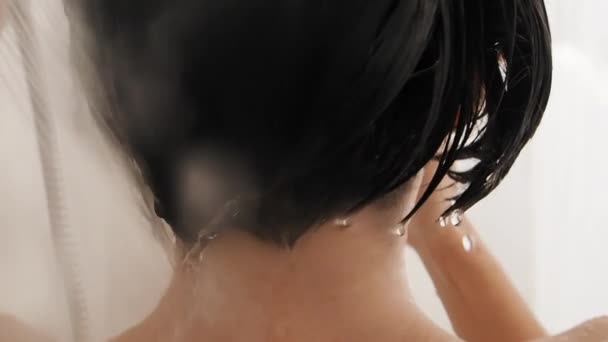 Naakte vrouw neemt een douche. Vrouw wast haar korte haar met shampoo. Slow motion video in witte badkamer. — Stockvideo