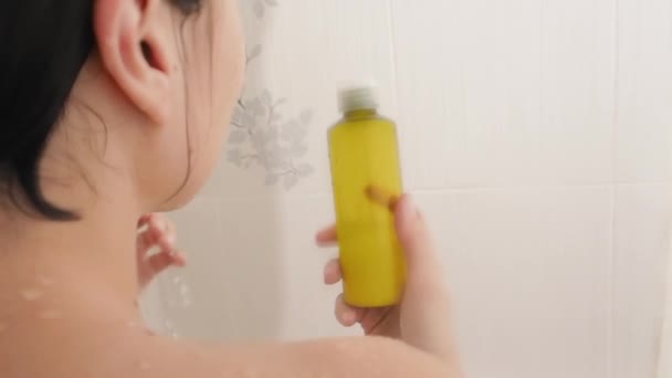 Naked woman takes a shower. Woman washes her short hair with shampoo from yellow botltle. Slow motion video in white bathroom. — Stock Video