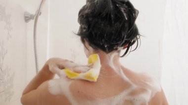 Kısa saçlı çıplak kadın komik sarı plastik ördekle duş alıyor. Kadın omuzlarını sarı süngerle yıkıyor. Beyaz banyo..