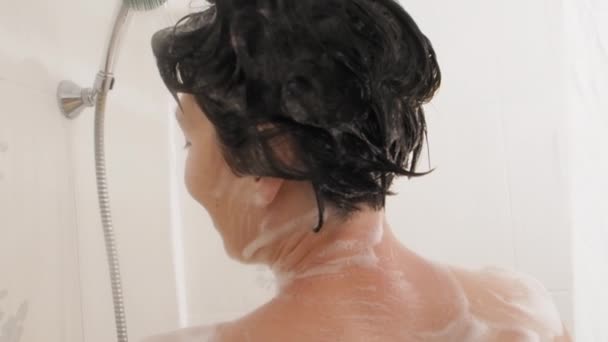 Naked woman with short hair takes a shower. Woman washes her shoulders with yellow sponge. White bathroom. — Stok video