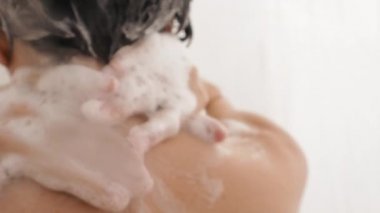 Naked woman takes a shower. Woman washes her short hair with shampoo. Slow motion video in white bathroom.