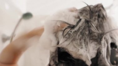 Naked woman takes a shower. Woman washes her short hair with shampoo. Slow motion video in white bathroom.