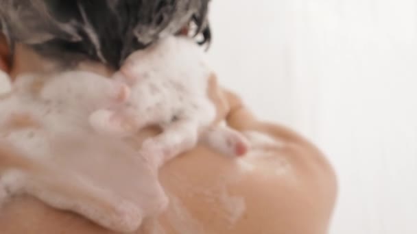 Naakte vrouw neemt een douche. Vrouw wast haar korte haar met shampoo. Slow motion video in witte badkamer. — Stockvideo